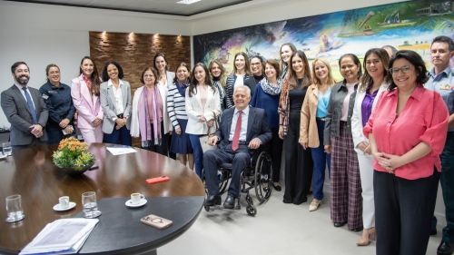 A group of diverse individuals, including a man in a wheelchair, poses together in a conference room with a colorful mural in the background.